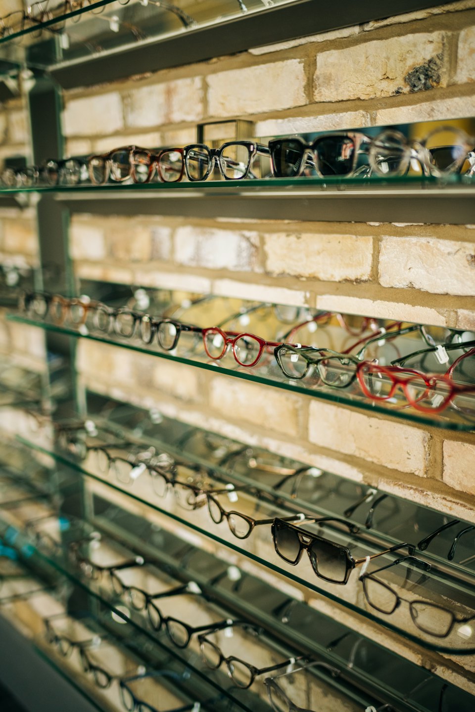 Various prescription eyeglasses displayed on clear shelves against a brick wall.